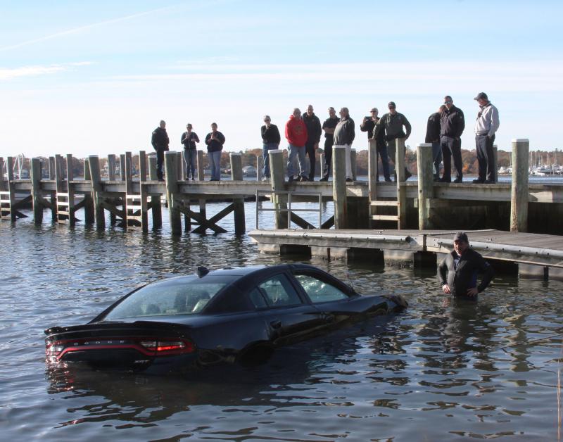 Onlookers gather on dock at Tempest Knob while a new Dodge is towed out of the water in November. The car’s owners said it slipped into the bay before they went fishing. BY MATTHEW BERNAT